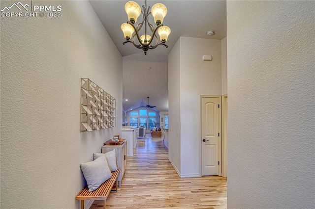 corridor with high vaulted ceiling, light hardwood / wood-style flooring, and an inviting chandelier