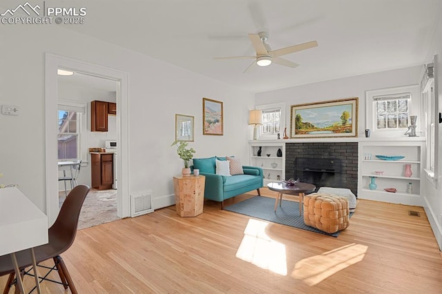 living room with ceiling fan, a brick fireplace, light wood-type flooring, and a wealth of natural light