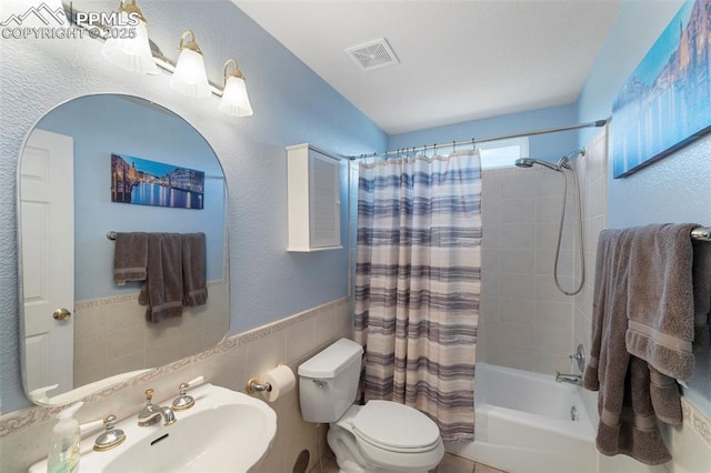 full bathroom featuring toilet, tile walls, shower / bath combo with shower curtain, and sink