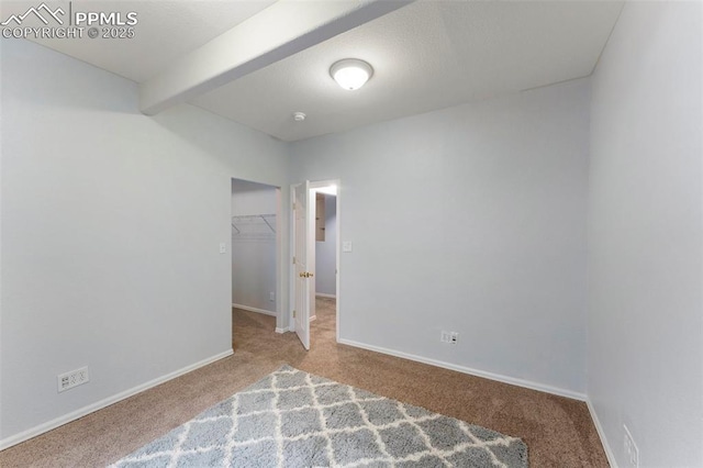 unfurnished bedroom featuring carpet flooring, a walk in closet, a closet, and beamed ceiling