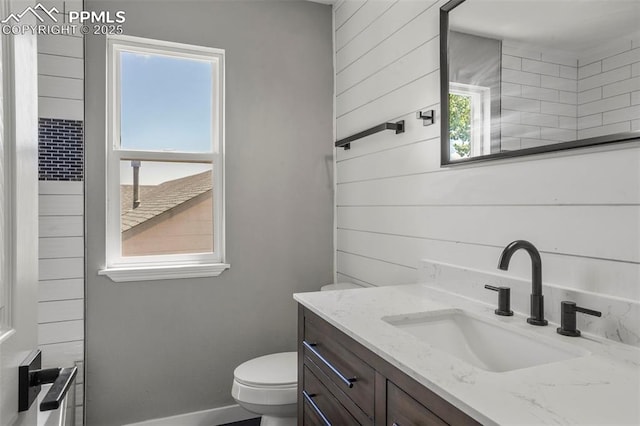 bathroom featuring wooden walls, vanity, and toilet