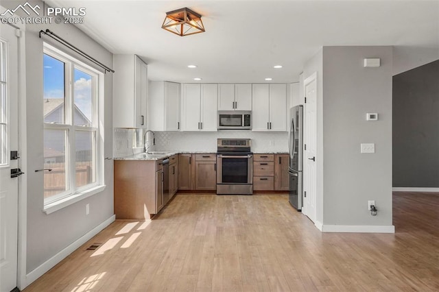 kitchen featuring light stone countertops, appliances with stainless steel finishes, backsplash, sink, and white cabinetry