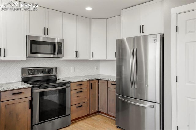 kitchen featuring light stone countertops, appliances with stainless steel finishes, tasteful backsplash, light hardwood / wood-style floors, and white cabinetry