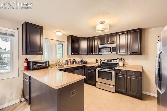 kitchen with kitchen peninsula, dark brown cabinetry, stainless steel appliances, sink, and light tile patterned flooring