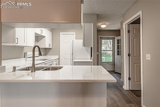 kitchen with dark hardwood / wood-style flooring, kitchen peninsula, a textured ceiling, white appliances, and white cabinets