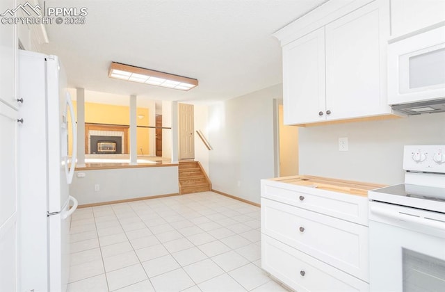 kitchen featuring white cabinetry, light tile patterned floors, white appliances, and a tile fireplace