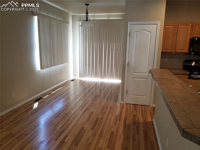 kitchen with decorative backsplash, light wood-type flooring, black appliances, pendant lighting, and tile countertops