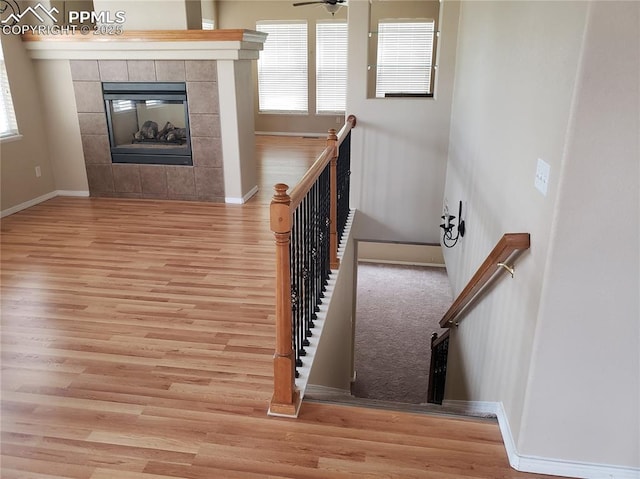 staircase featuring wood-type flooring, ceiling fan, and a tiled fireplace