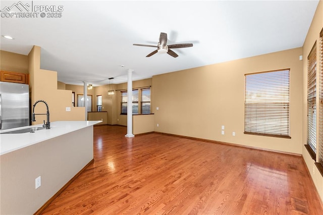 unfurnished living room featuring ornate columns, sink, ceiling fan with notable chandelier, and light wood-type flooring