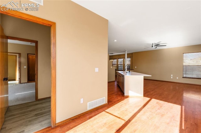 interior space with wood-type flooring, ceiling fan, a kitchen island with sink, and sink