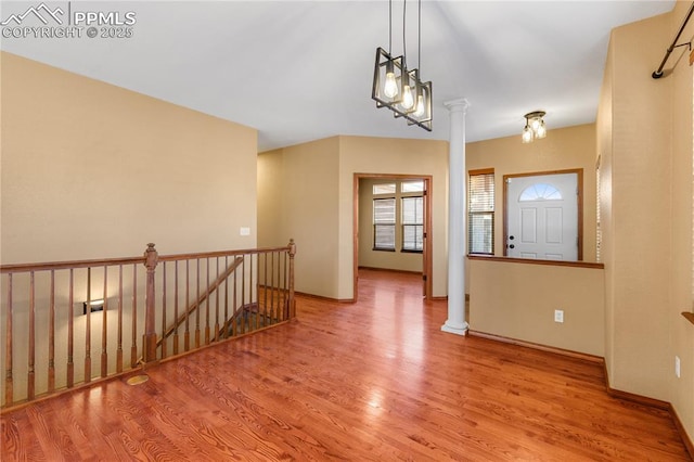 foyer entrance with light hardwood / wood-style floors, decorative columns, and a notable chandelier