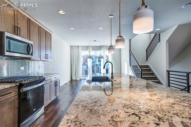 kitchen with decorative backsplash, appliances with stainless steel finishes, light stone counters, a textured ceiling, and pendant lighting