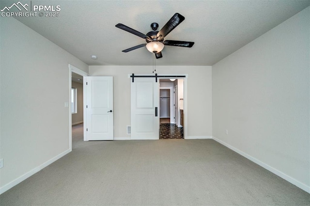 unfurnished bedroom featuring a barn door, carpet floors, and ceiling fan