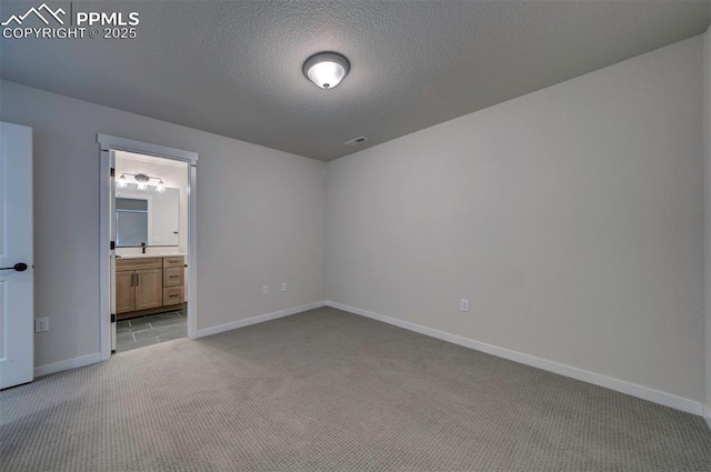 unfurnished bedroom with ensuite bath, light colored carpet, and a textured ceiling