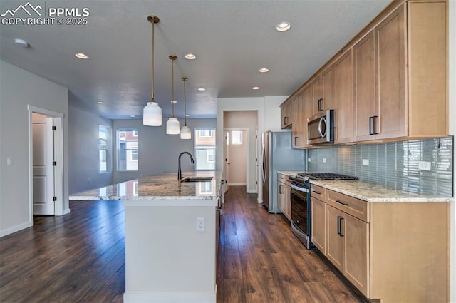 kitchen with light stone countertops, sink, hanging light fixtures, stainless steel appliances, and a center island with sink