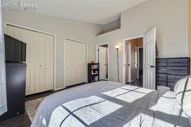 bedroom with vaulted ceiling, two closets, and dark hardwood / wood-style flooring