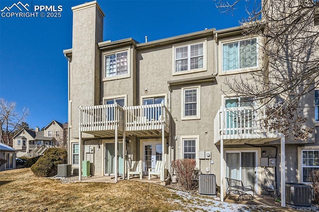 back of property with central AC unit, a lawn, and a balcony