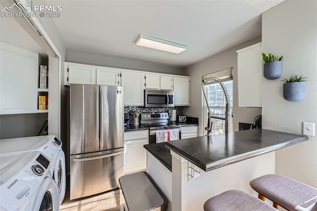 kitchen featuring white cabinetry, appliances with stainless steel finishes, a kitchen bar, and washing machine and dryer