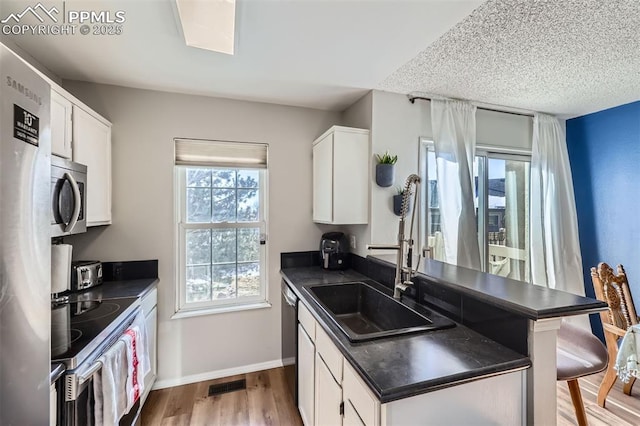 kitchen with sink, a breakfast bar area, appliances with stainless steel finishes, white cabinetry, and light wood-type flooring