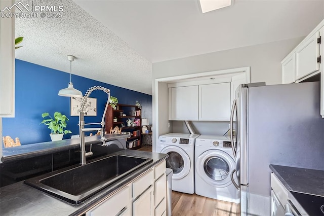 laundry room featuring washing machine and clothes dryer, sink, cabinets, a textured ceiling, and light wood-type flooring