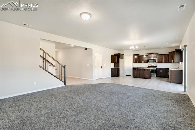 unfurnished living room with light carpet, sink, and an inviting chandelier