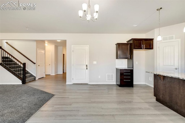 kitchen with light stone counters, dark brown cabinets, a notable chandelier, light hardwood / wood-style floors, and hanging light fixtures