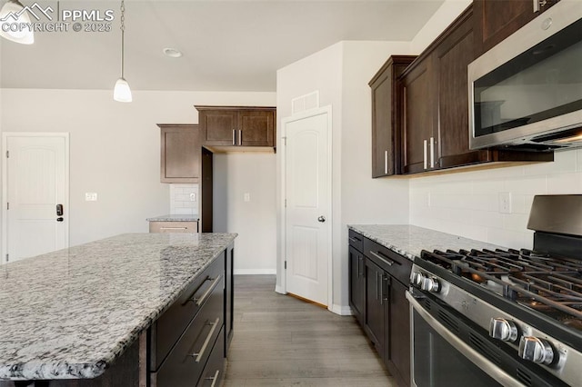 kitchen with dark wood-type flooring, hanging light fixtures, a kitchen island, light stone counters, and stainless steel appliances