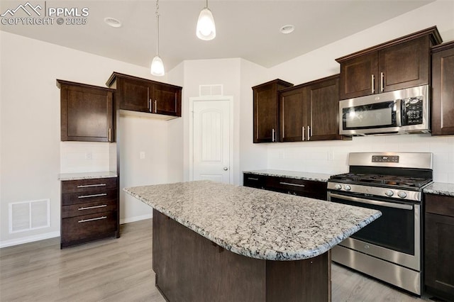 kitchen featuring light wood-type flooring, dark brown cabinets, stainless steel appliances, a kitchen island, and hanging light fixtures