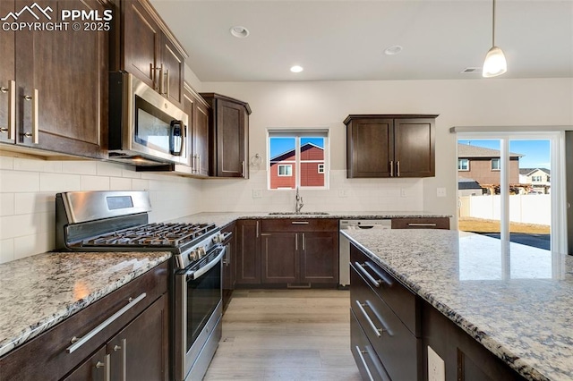 kitchen featuring light stone countertops, stainless steel appliances, sink, light hardwood / wood-style floors, and hanging light fixtures