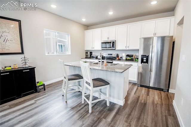 kitchen with a kitchen island with sink, white cabinets, sink, light stone counters, and stainless steel appliances