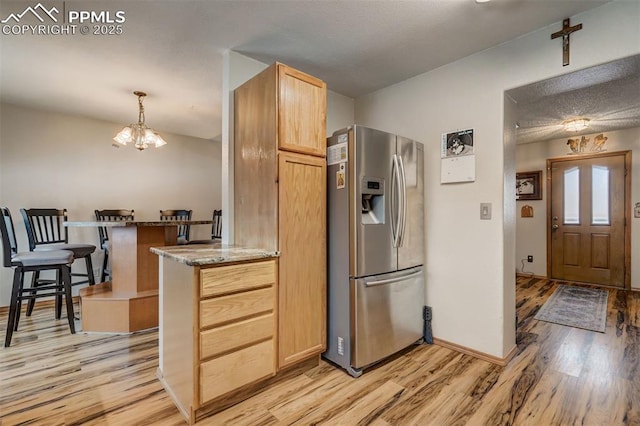 kitchen with light brown cabinetry, light stone counters, stainless steel fridge with ice dispenser, kitchen peninsula, and light hardwood / wood-style floors