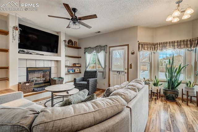 living room featuring ceiling fan with notable chandelier, a fireplace, a textured ceiling, and light hardwood / wood-style flooring