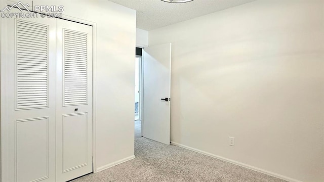 unfurnished bedroom featuring a textured ceiling, light colored carpet, and a closet