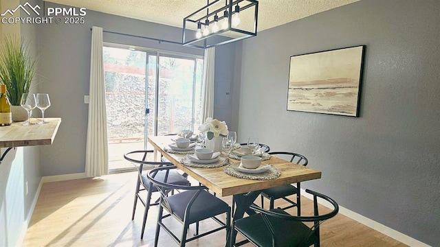 dining space with light hardwood / wood-style flooring, a textured ceiling, and a notable chandelier