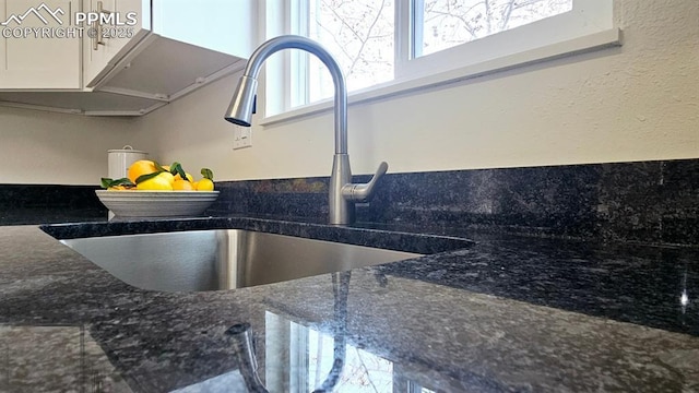 interior details featuring white cabinets, dark stone countertops, and sink