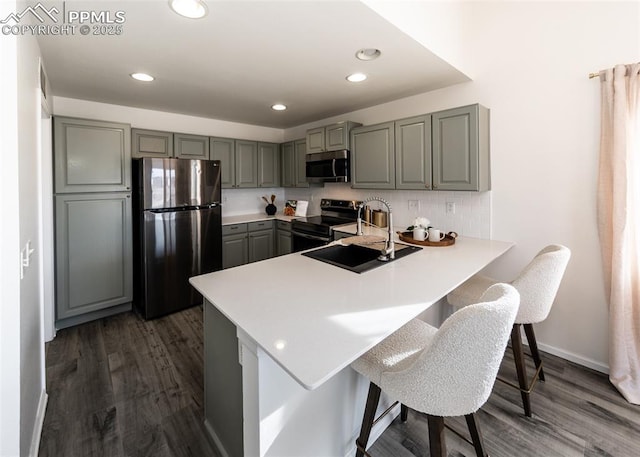 kitchen with a kitchen breakfast bar, sink, dark hardwood / wood-style floors, kitchen peninsula, and stainless steel appliances