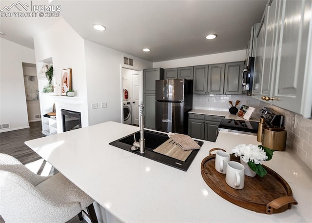 kitchen featuring kitchen peninsula, appliances with stainless steel finishes, tasteful backsplash, washer / dryer, and gray cabinets