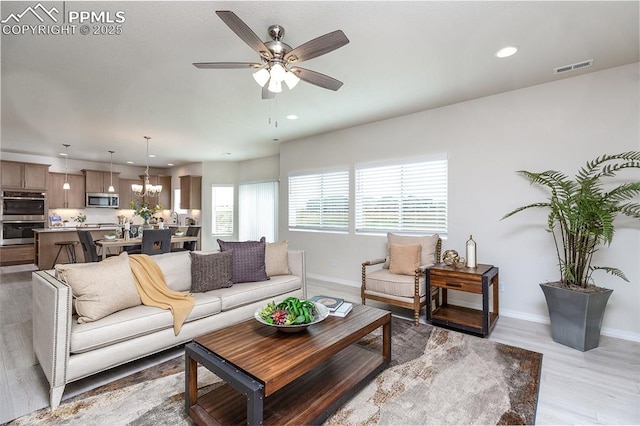 living room with ceiling fan with notable chandelier and light hardwood / wood-style floors