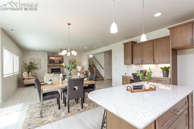 kitchen featuring decorative light fixtures, a stone fireplace, light stone countertops, and a kitchen island with sink