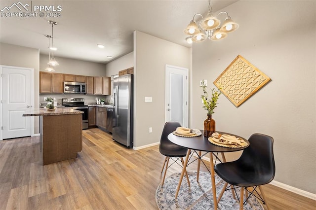 kitchen with light hardwood / wood-style flooring, a kitchen island, a notable chandelier, appliances with stainless steel finishes, and pendant lighting