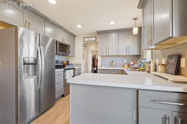 kitchen with stainless steel appliances, light hardwood / wood-style floors, backsplash, hanging light fixtures, and gray cabinetry