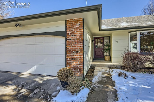 snow covered property entrance featuring a garage