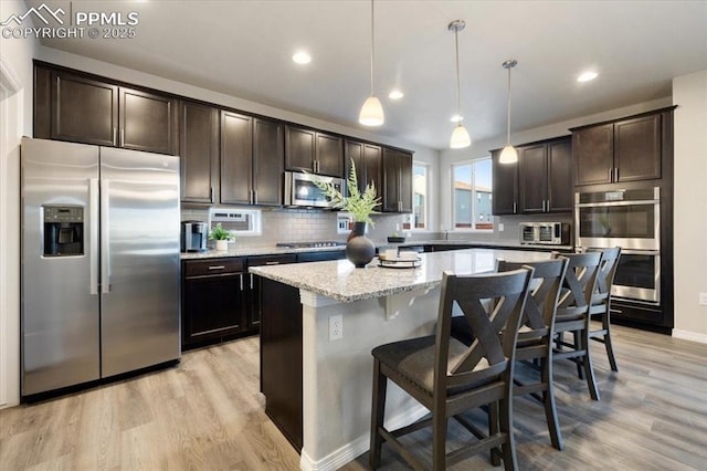 kitchen with stainless steel appliances, a center island, light stone counters, light wood-type flooring, and hanging light fixtures