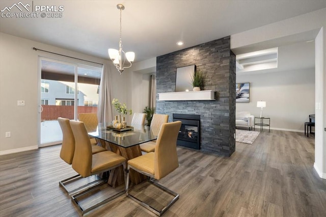 dining space with a stone fireplace, a chandelier, and hardwood / wood-style floors