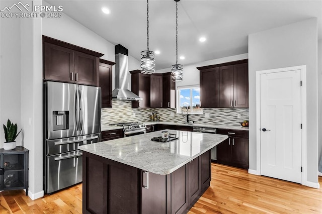 kitchen with appliances with stainless steel finishes, wall chimney exhaust hood, decorative light fixtures, a kitchen island, and a breakfast bar area