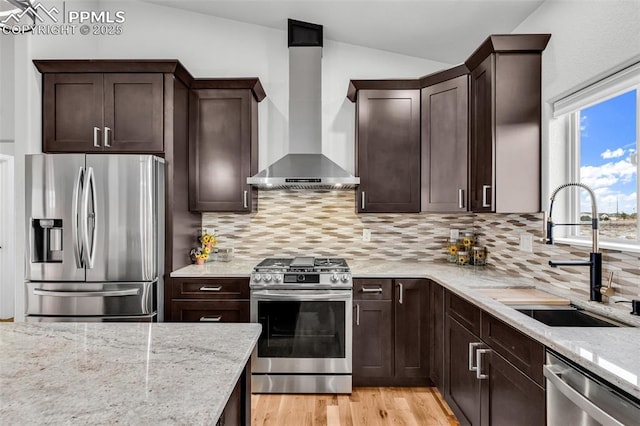 kitchen with appliances with stainless steel finishes, sink, lofted ceiling, and wall chimney range hood