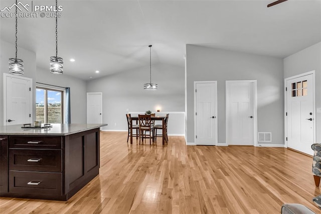 kitchen featuring vaulted ceiling, dark brown cabinetry, light hardwood / wood-style floors, and decorative light fixtures