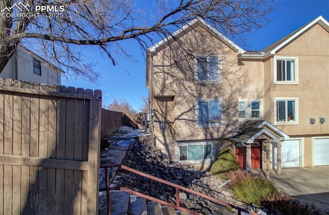 view of front of house with a garage, concrete driveway, fence, and stucco siding