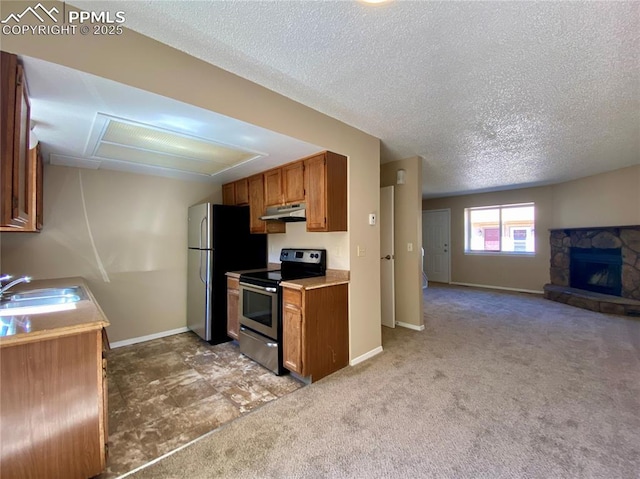 kitchen featuring a stone fireplace, sink, a textured ceiling, light colored carpet, and stainless steel appliances