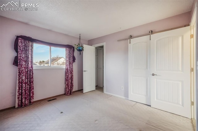 unfurnished bedroom with a barn door and light colored carpet